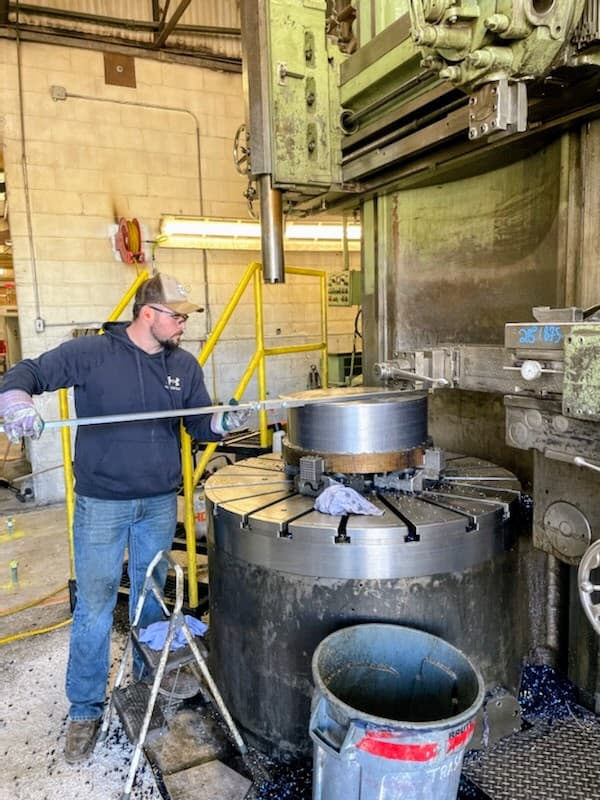 Machinist measuring a large cylindrical part on a vertical turret lathe
